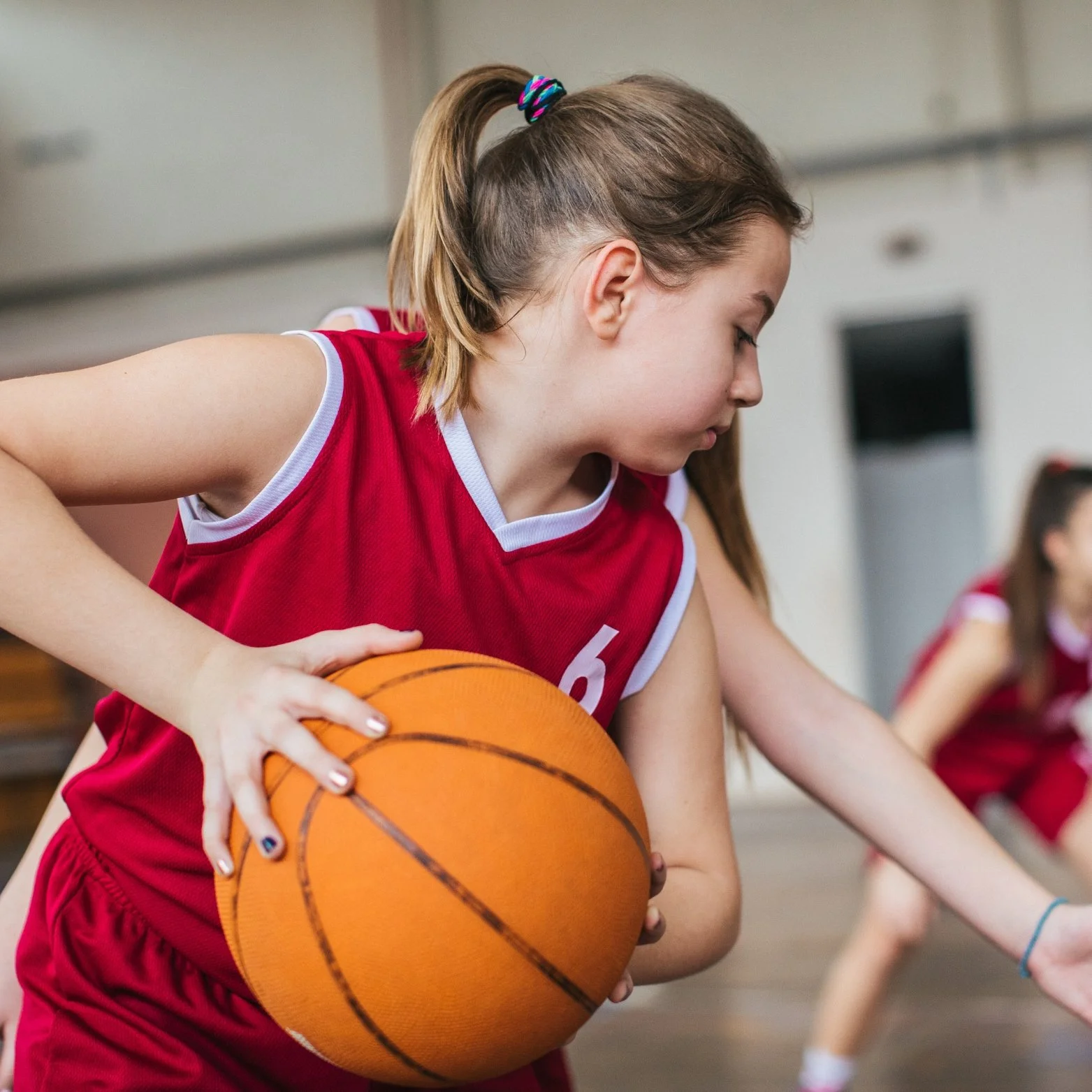 Young girl in red sports uniform playing basketball.