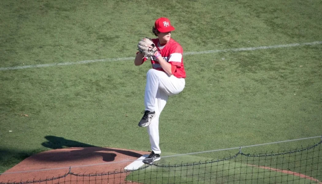 Youth baseball game with three players on the field, one pitcher preparing to throw, in a park with green trees in the background.