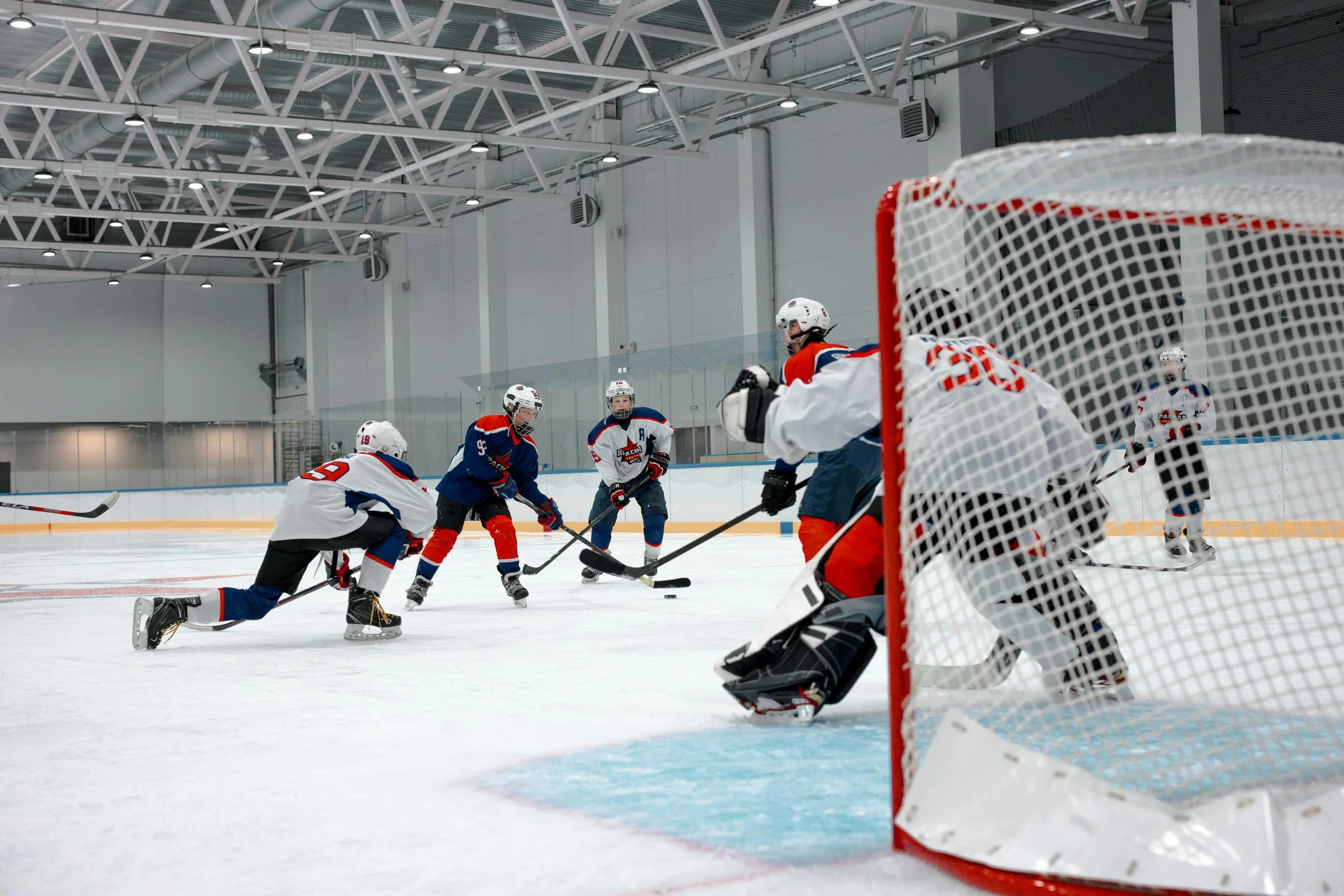 An ice hockey game underway with players from two teams chasing the puck near the goal, fans watching from the stands.