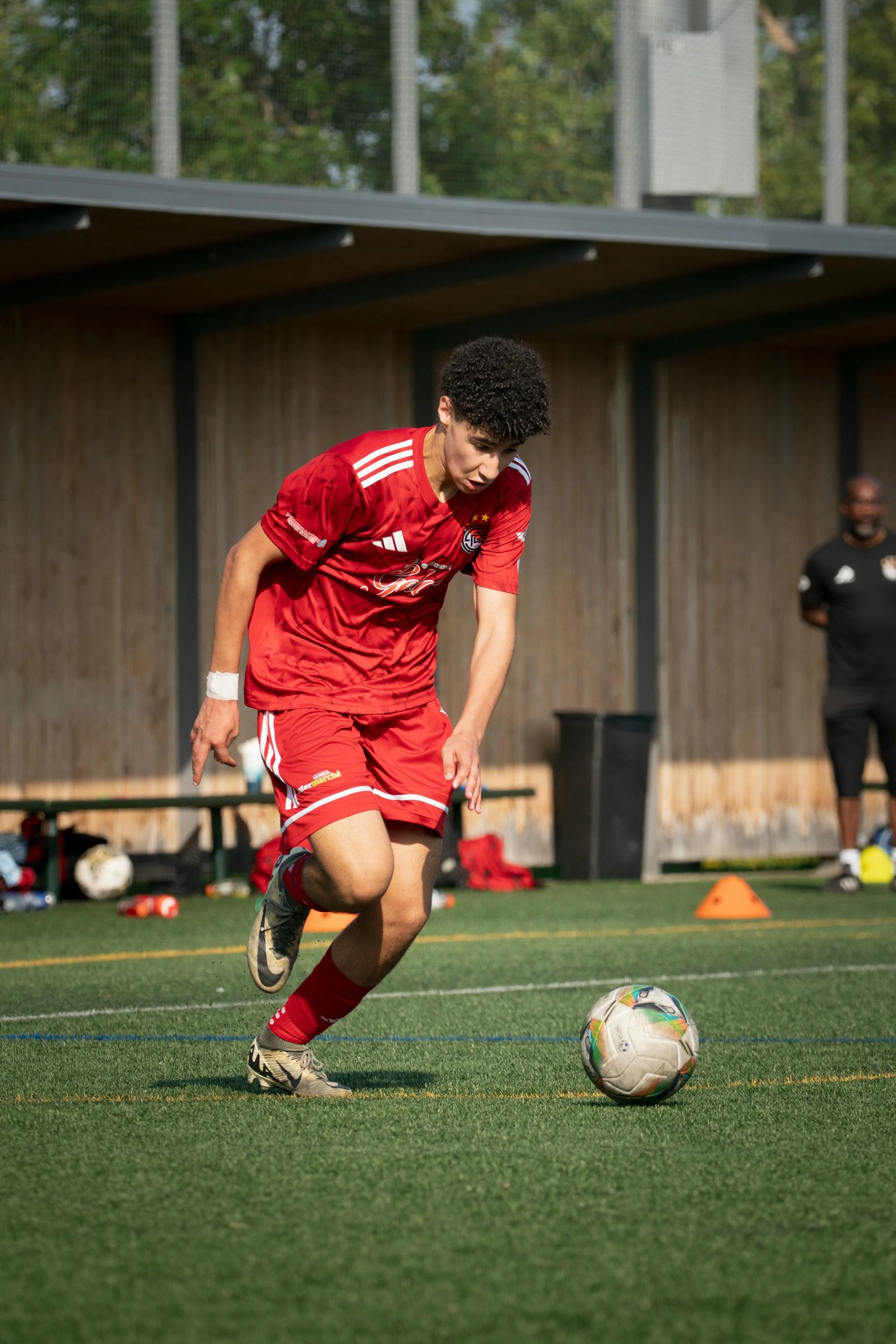 Young male soccer player in red uniform controlling the ball on the field during practice or game.