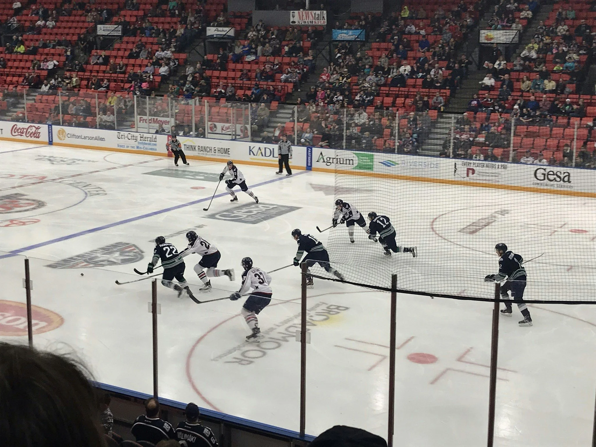 Hockey players in action during a game at an indoor arena with viewers seated in the background.