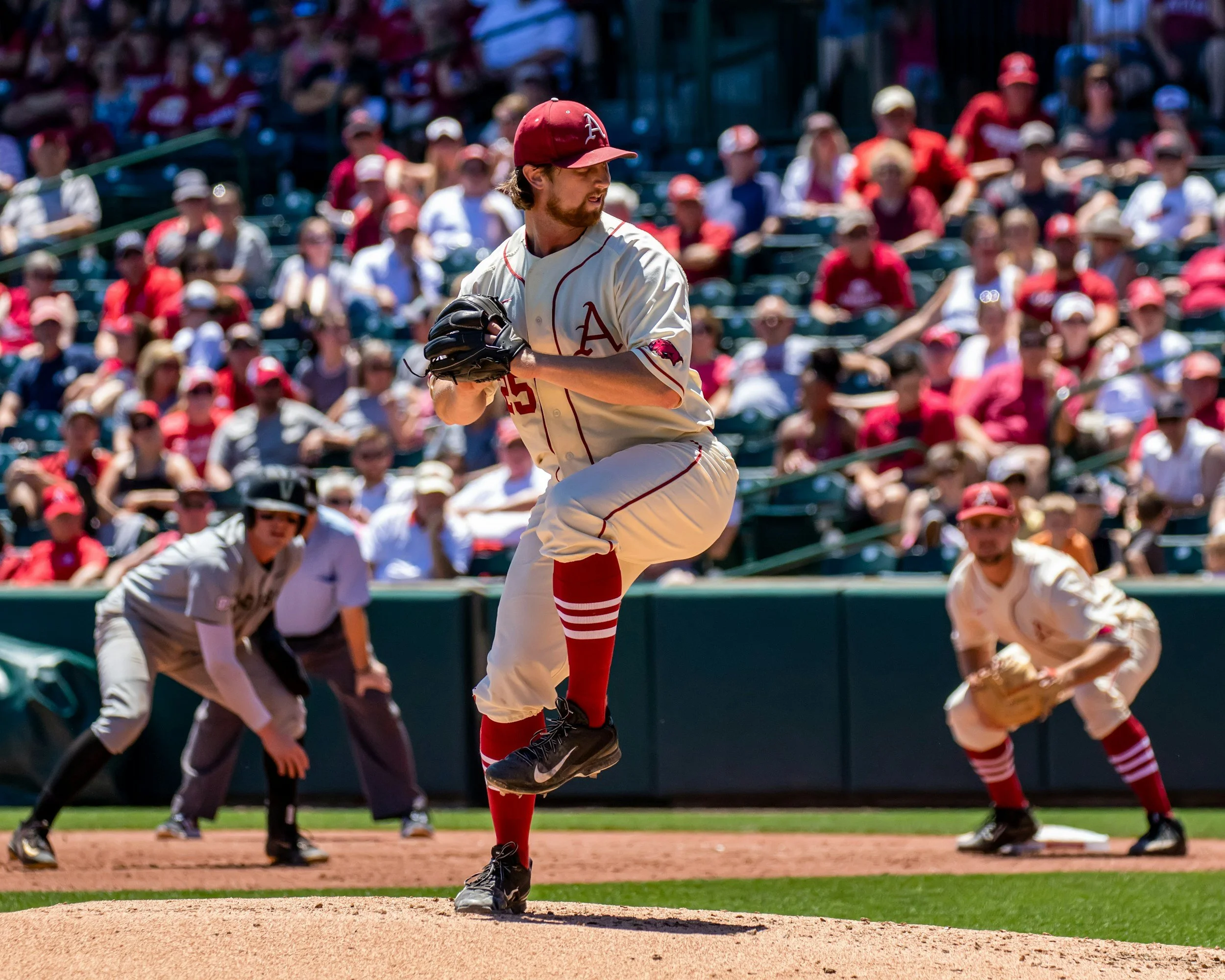 A baseball player in a white uniform with red accents is pitching on the mound during a game. The crowd in the stands is mostly dressed in red and white, watching the game.