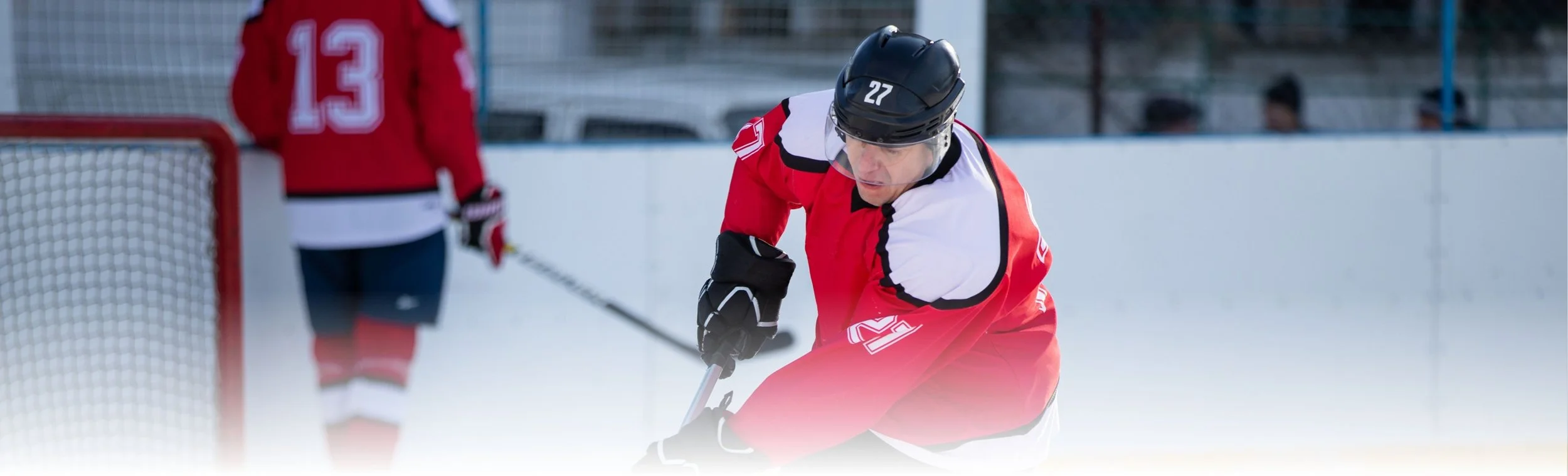 Hockey player in red uniform and black helmet bending forward on ice rink during game.